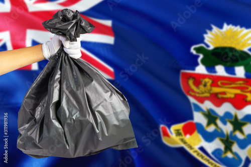 Cayman Islands environmental protection concept. The male hand holding a garbage bag on national flag background. Ecological and recycling theme with copy space.