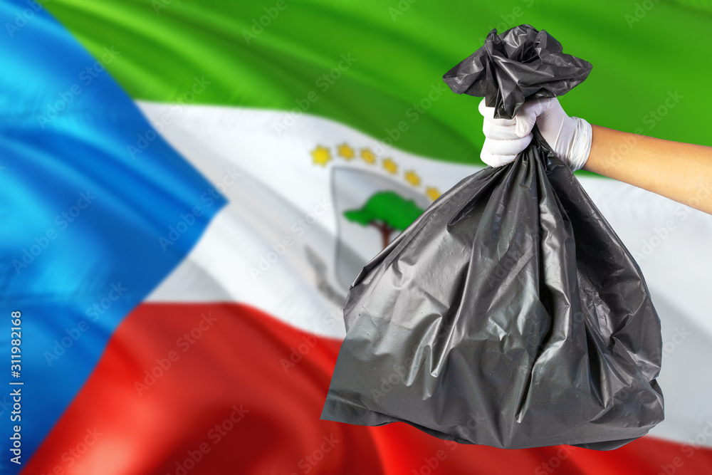 Equatorial Guinea environmental protection concept. The male hand holding a garbage bag on national flag background. Ecological and recycling theme with copy space.