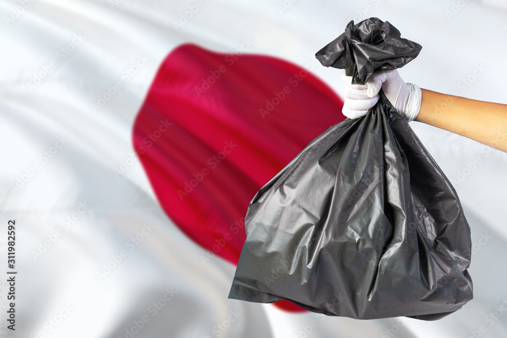 Japan environmental protection concept. The male hand holding a garbage bag on national flag background. Ecological and recycling theme with copy space.