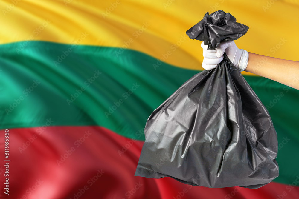 Lithuania environmental protection concept. The male hand holding a garbage bag on national flag background. Ecological and recycling theme with copy space.
