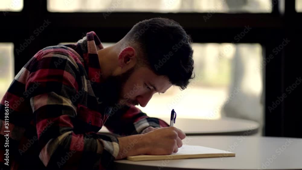A Young Man Wearing Red Long Sleeve Writing On His Notes in the Table - Close-Up Shot A Young Man Wearing Red Long Sleeve Writing On His Notes in the Table - Close-Up Shot
