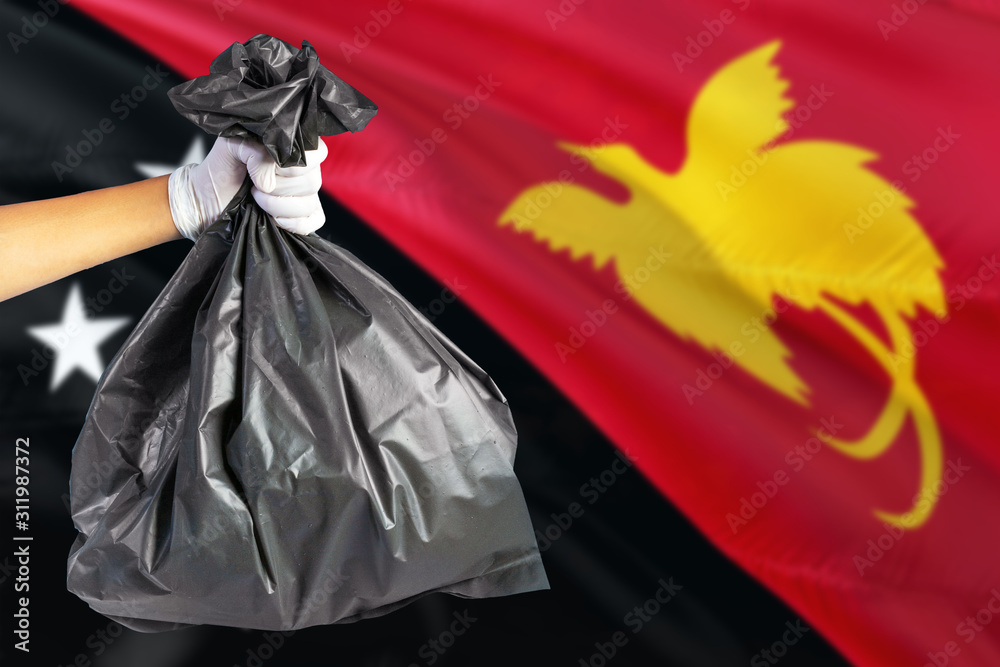 Papua New Guinea environmental protection concept. The male hand holding a garbage bag on national flag background. Ecological and recycling theme with copy space.