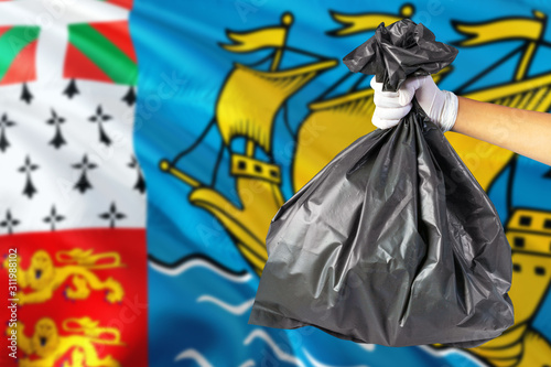 Saint Pierre And Miquelon environmental protection concept. The male hand holding a garbage bag on national flag background. Ecological and recycling theme with copy space.