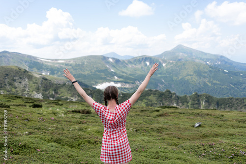 The girl stands in the background of the mountains and raises her hands up