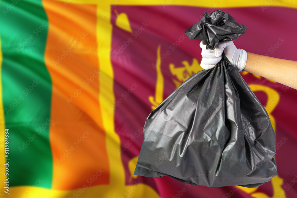 Sri Lanka environmental protection concept. The male hand holding a garbage bag on national flag background. Ecological and recycling theme with copy space.