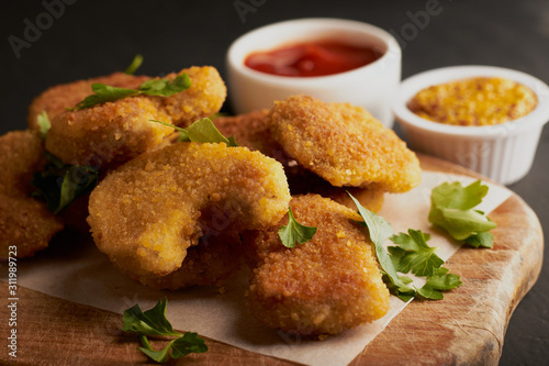 Close-up of chicken nuggets on a cutting board and tomato chili sauce with mustard seeds on a dark background