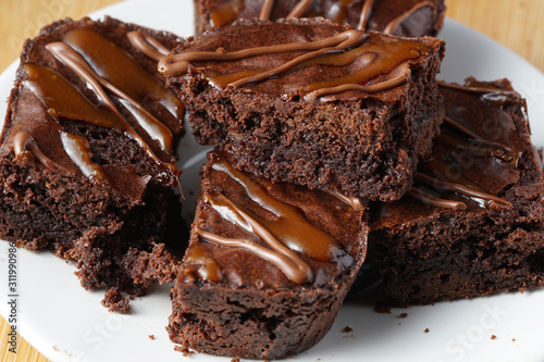 Close up of delicious dark fudgy brownies serve on round white plate ove wooden table.