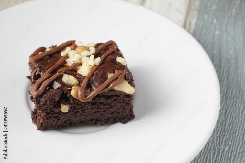 Close up on top of moist dark chocolate brownie with mix nut on top served on white round plate over vintage background Close up on top of moist dark chocolate brownie with mix nut on top served on white round plate over vintage background