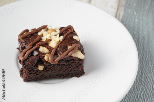 Close up on top of  moist dark chocolate brownie with mix nut on top served on white round plate over vintage background