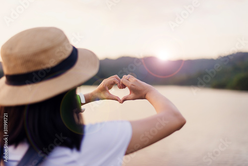 Woman standing and showing hands heart shape at sunset