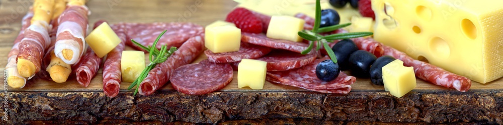 Meat and cheese plate antipasti snack with Prosciutto ham, Parmesan, Blue cheese, Cantaloupe melon and Olives on olive wood serving board. panoramic shot