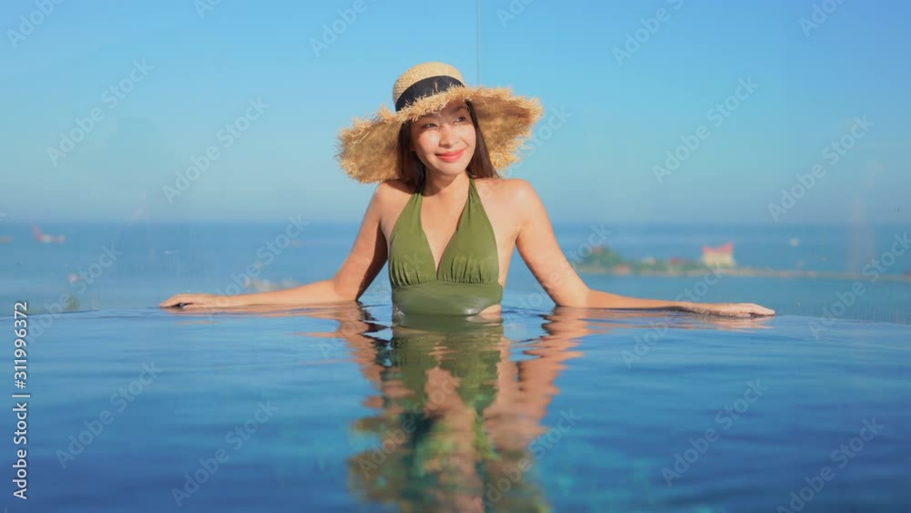 Young pretty Asian woman relaxing at the edge of a resort infinity pool is mirror-imaged in the pool waters. Young pretty Asian woman relaxing at the edge of a resort infinity pool is mirror-imaged in the pool waters.