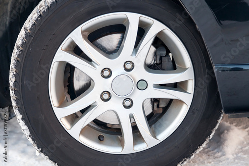 An aluminum alloy wheel with winter studded tires on a black car with a poorly worn brake disk requiring replacement. Weather and transport. Auto service industry.