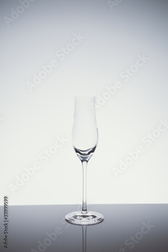 Liqueur glass on the light background.. Fine cristal glassware concept. Vertical, cold tone in light cold toning