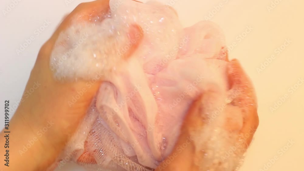 Female hand holds pink washcloth with soap foam on white background Female hand holds pink washcloth with soap foam on white background