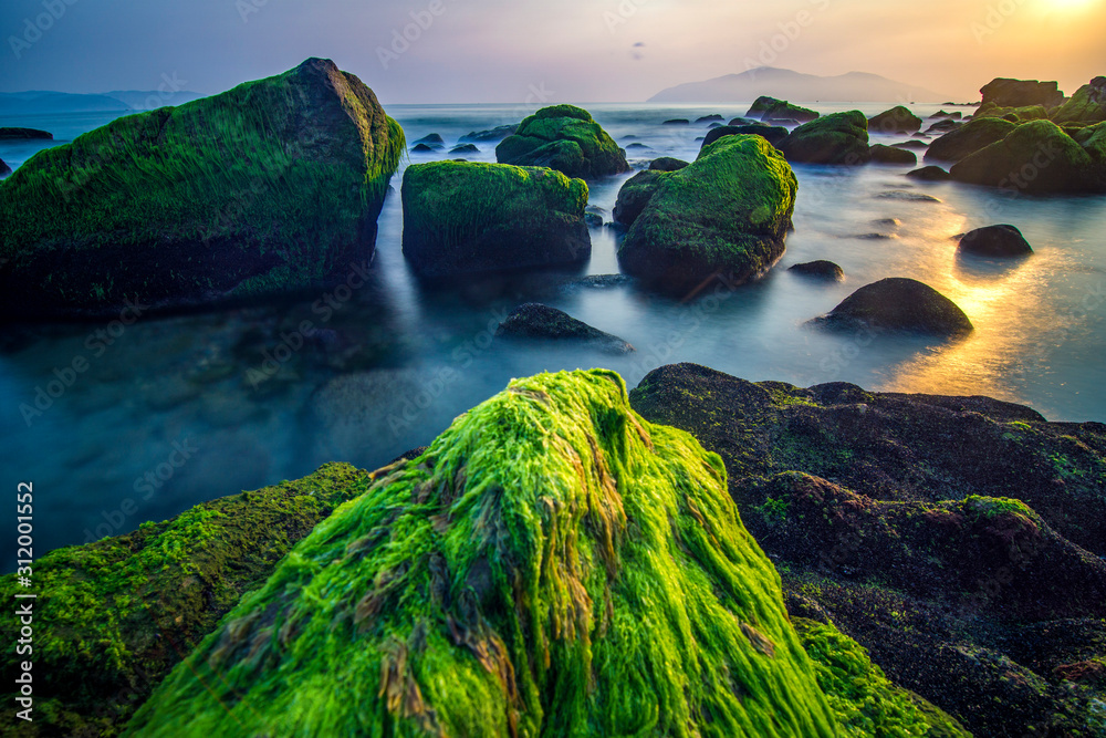 Da Nang beach with moss rocks and waves at sunrise.