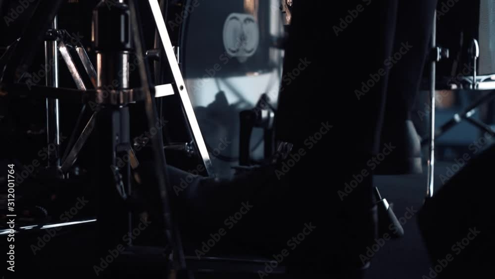 Close-up of the legs of a drummer in shoes on stage. The drummer kicks the bass drum pedal. A man plays the drums in a musical group, live performance.