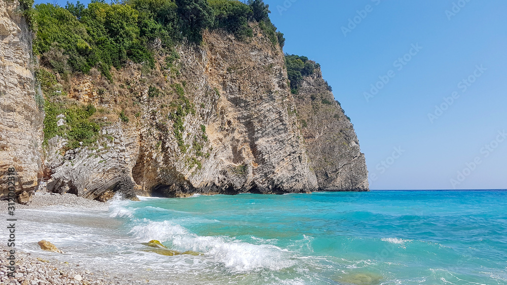 Panoramic view of pebble beach with clear azure blue water and layered rocks, beautiful mediterranean Adriatic Sea coast, Montenegro, selective focus