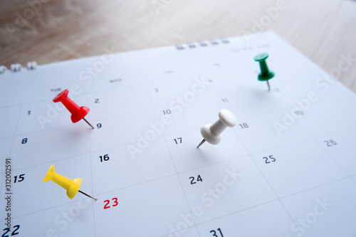 Thumbtack a date on calendar on the table with wooden background, concept for important date, meeting reminder, planning for business, travel planning concept