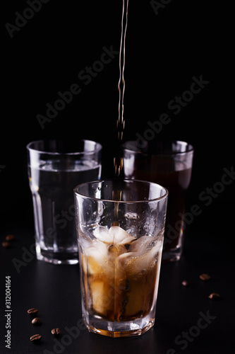 coffee is poured into a glass with ice. refreshing drink on a black background