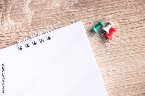 Top view of white blank paper desk spiral calendar with colorful pins on wooden background