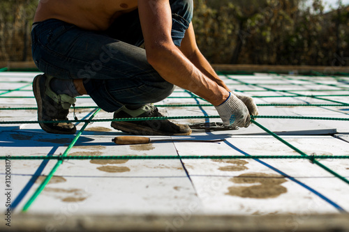 Worker hands knitting metal rebar closeup before pouring concrete. Steel reinforcement of basement slab. Contractor fixing armature in the house formwork (falsework). Foundation installing works