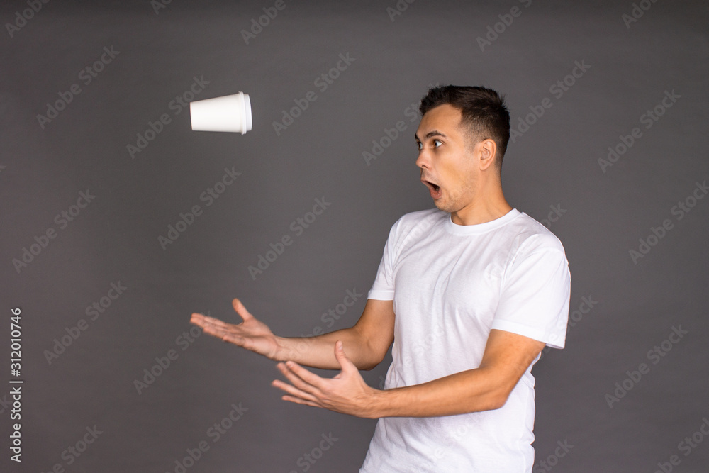 A guy in a white t-shirt juggles glasses of coffee, drops them on the ground. A guy in a white t-shirt juggles glasses of coffee, drops them on the ground.
