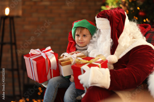 Santa Claus and little boy with Christmas gifts indoors
