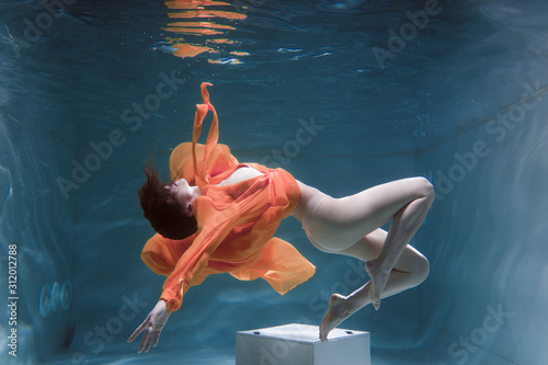 Beautiful girl swims underwater in a yellow dress. 2020 New Year trend Aqua Mente and fatom blue and lush lava. Underwater girl mermaid. Model suitable for advertising