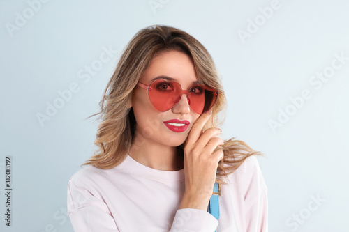 Young woman wearing heart shaped sunglasses on light grey background © New Africa