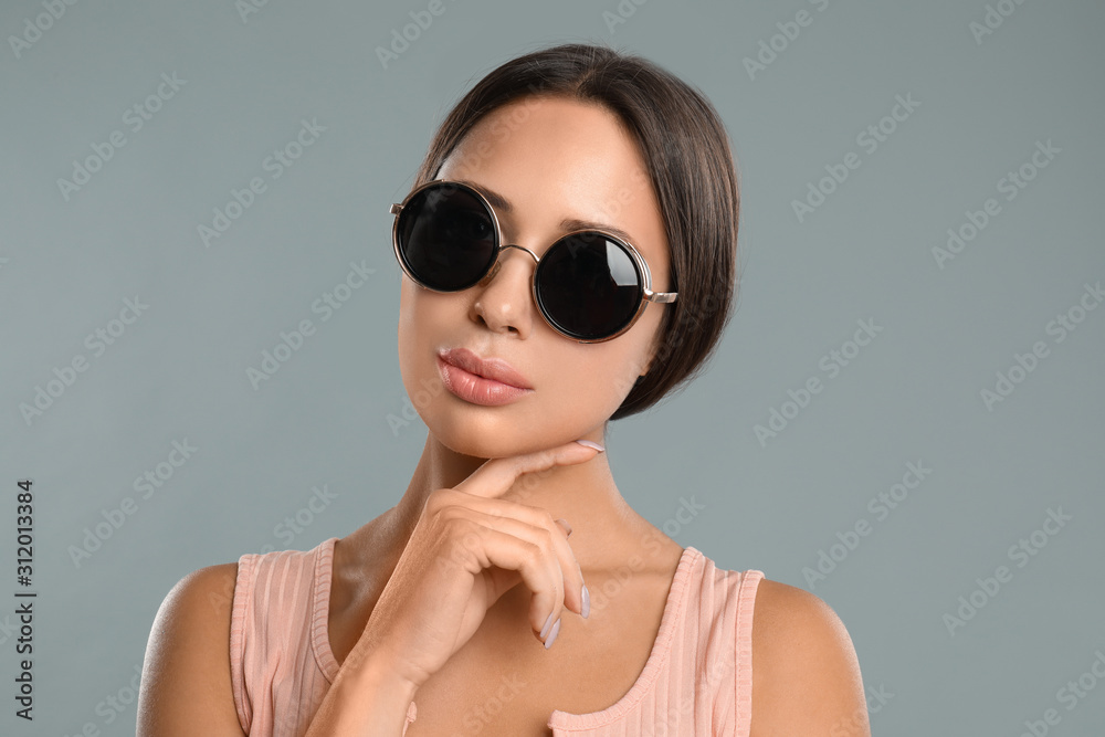 Beautiful young woman wearing sunglasses on grey background Beautiful young woman wearing sunglasses on grey background