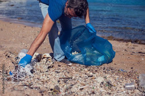 Man volunteer with big bag for trash collecting garbage on beach. Environmental pollution concept © Aleksej