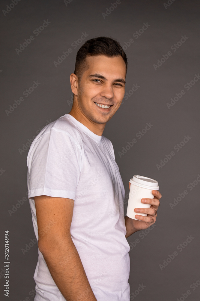 A guy in a white t-shirt is holding glasses of coffee.