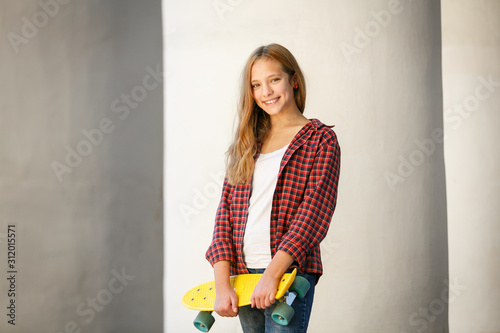 Lifestyle outdoor portrait of young smiling teenage girl with a yellow skateboard
