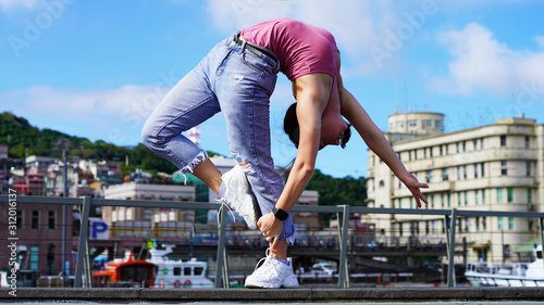 young beautiful flexible girl in the city on the embankment stands in a bridge pose. gymnast in life style clothes at the observation deck in the port does gymnastic elements. backbend pose. yachts