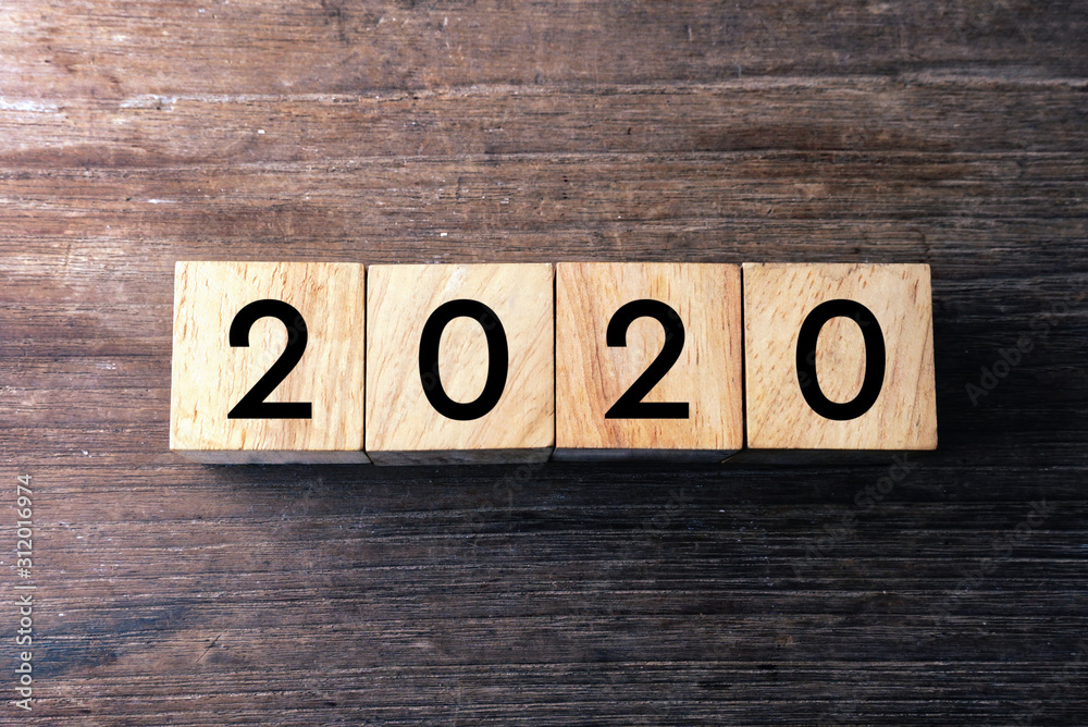 Fototapeta premium Top view text 2020 on wood cube which lay on wood table.