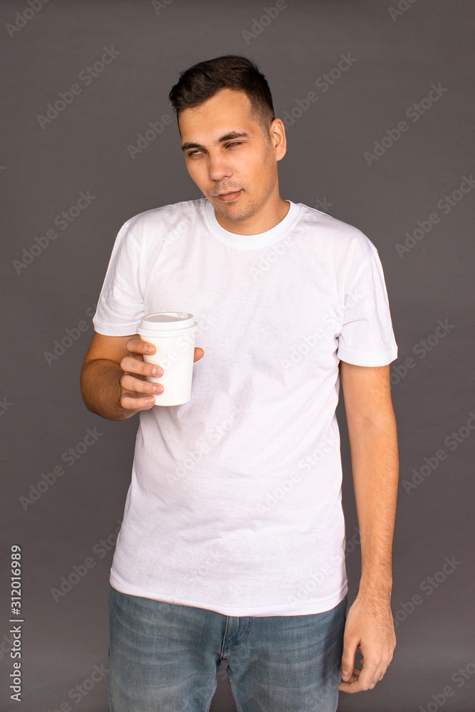 A guy in a white t-shirt is drinking coffee and trying to Wake up and cheer up.