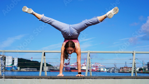 Young flexible girl in life style clothes makes a handstand on observation deck in the passenger port. beautiful gymnast twine on a background of blue sky on sunny day. back bend pose. Handstand poses