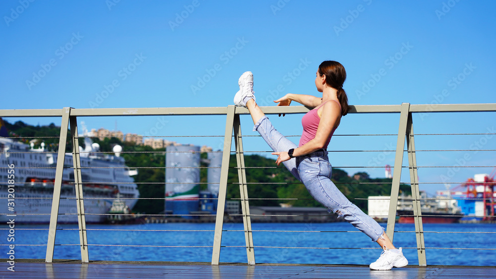 beautiful girl in life style denim clothes does twine on the railing in the port. dancer, gymnast, acrobat on sunny day in passenger port on background of cruise ship. twine on the observation deck beautiful girl in life style denim clothes does twine on the railing in the port. dancer, gymnast, acrobat on sunny day in passenger port on background of cruise ship. twine on the observation deck