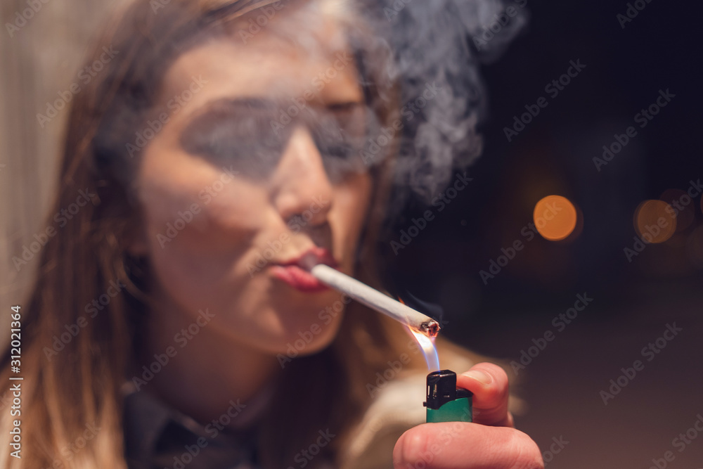 Obraz premium Close up portrait of young caucasian woman on the street at night lighting cigarette with lighter smoking in the city outdoor smoke