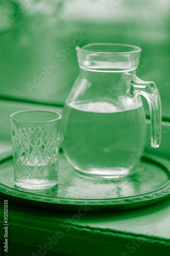 Jug of water and a glass on the windowsill, green tone.