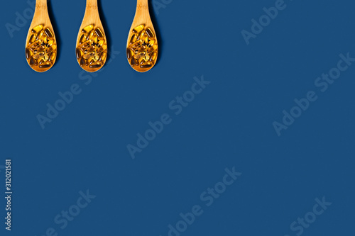 Medical classic blue background. Fish oil capsules in wooden spoons. Flat lay, top view.