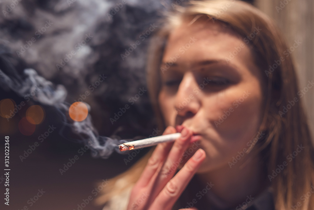Obraz premium Close up portrait of young caucasian woman smoker on the street at night with cigarette smoking in the city outdoor smoke enjoining