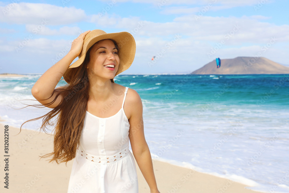 Happy cheerful young woman with straw hat walking on Corralejo Dunas beach in Fuerteventura island Happy cheerful young woman with straw hat walking on Corralejo Dunas beach in Fuerteventura island