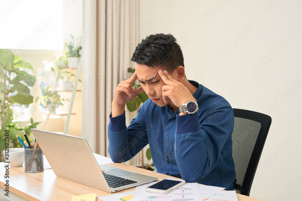 Feeling exhausted. Frustrated young beard man massaging his head and keeping eyes closed while sitting at his working place in office