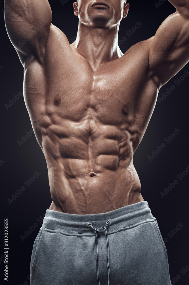 Fototapeta premium Close-up of a power fitness man's body. Handsome power athletic young man with great physique. Strong shirtless bodybuilder with six pack, perfect abs, shoulders, biceps, triceps and chest.