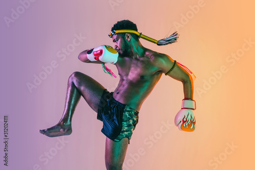 Muay thai. Young man exercising thai boxing on gradient background in neon light. Fighter practicing, training in martial arts in action, motion. Healthy lifestyle, sport, asian culture concept. photo