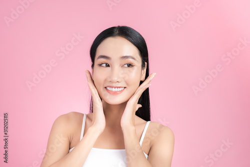 Beautiful young Asian girl touching her perfect skin on pink background. Skin care concept