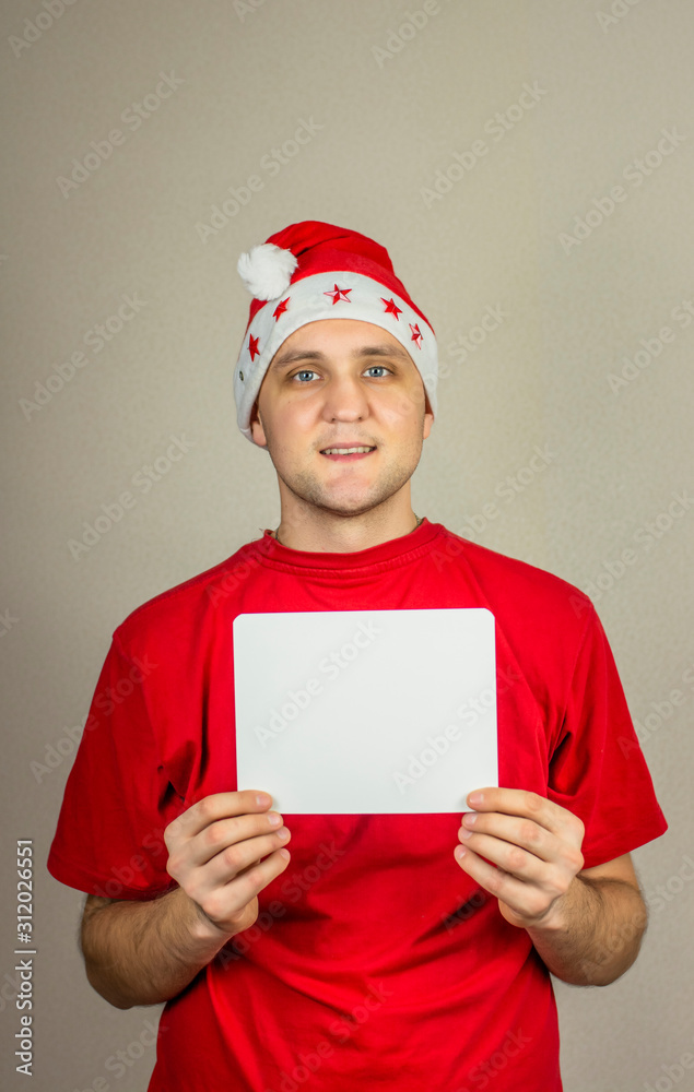 young guy in christmas hat and red t-shirt with white card in his hands for inscription young guy in christmas hat and red t-shirt with white card in his hands for inscription