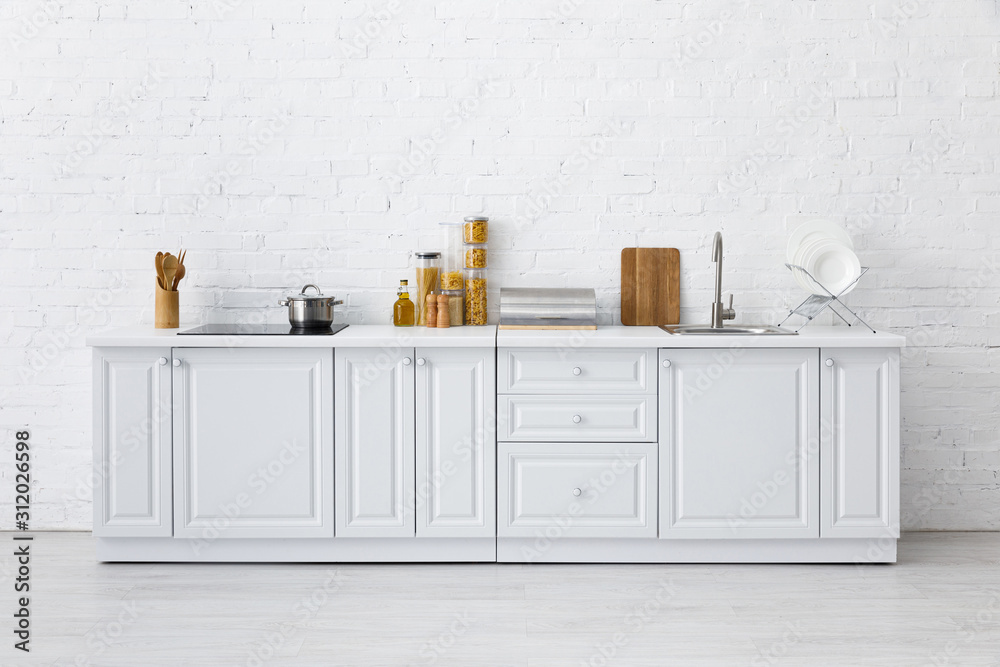 minimalistic modern white kitchen interior with kitchenware near brick wall - obrazy, fototapety, plakaty 